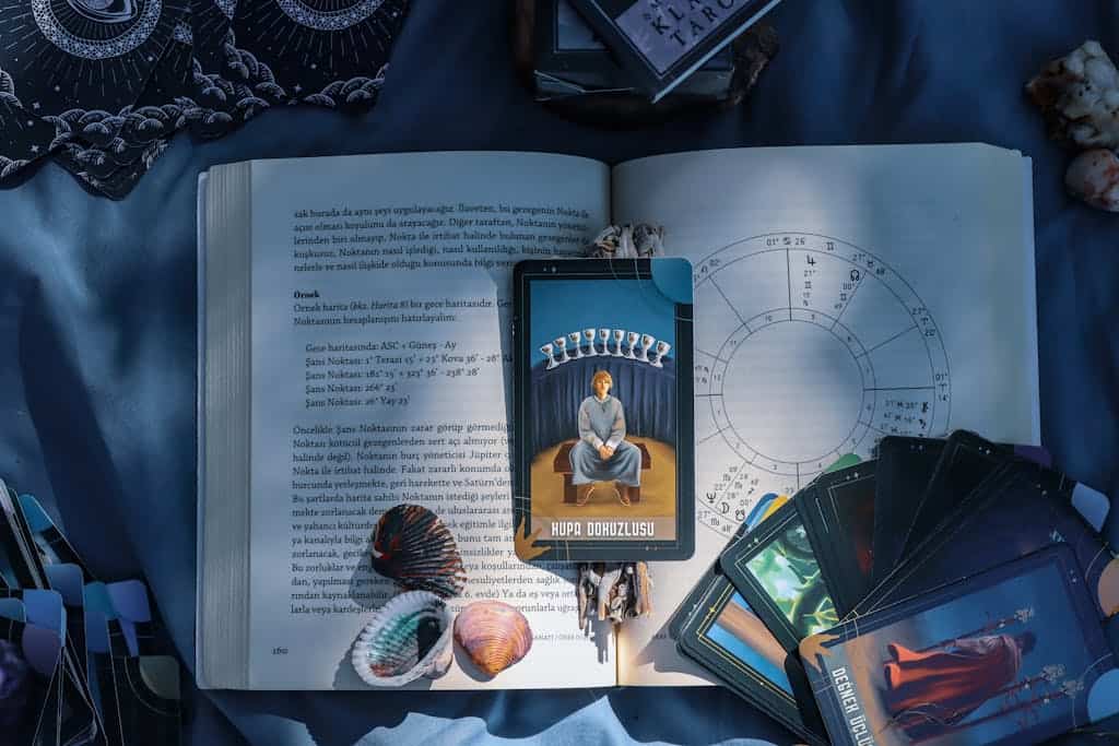 An artistic flat lay of tarot cards and astrology on a book with seashells, featuring Kupa Dokuzlusu card.