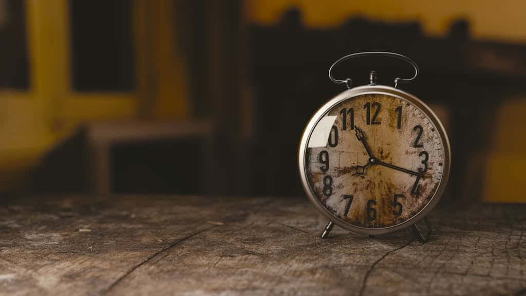 A classic vintage alarm clock sits on a rustic wooden table indoors.